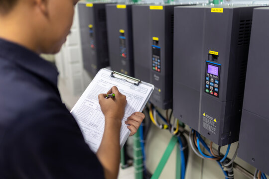 Inverter Control Room System Electrical engineers monitor the controller's frequency and current and record the data to the paper in his hand.