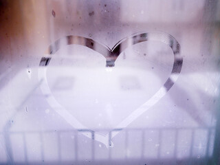 heart is painted on the misted glass of window in the winter time