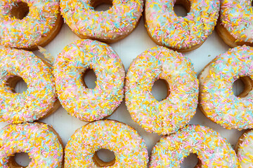 A box of glazed ring doughnuts with white frosting and colourful sprinkles