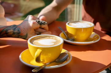 Close up selective focus coffee cups with hearts and hands of man and woman touching each other.
