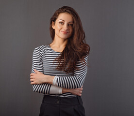 Obraz premium Beautiful natural happy smiling woman with long brown healthy hair style with folded arms. Healthy lifestyle and success business. Closeup portrait on grey background