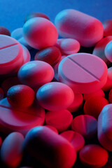 Extasy and drug concept. Close up shot of white and colored pills of different kind lit with red and blue neon lights.
