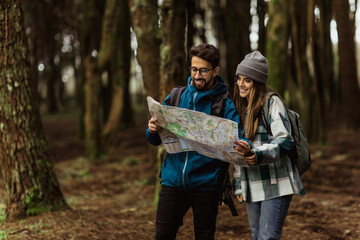 Happy millennial caucasian woman and man in jacket with backpack resting in cold forest looking at map