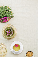 Fototapeta na wymiar Herbal tea from kipreya leaves in white cups on linen fabric table background, fireweed green leaves and flowers on wooden tray. Flavored herbal tea from wild plants, healing hot beverage.