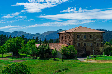 Fototapeta na wymiar An old brick manor with 3 floors and a tiled roof against the backdrop of mountains and green grass. Basque Country, Spain