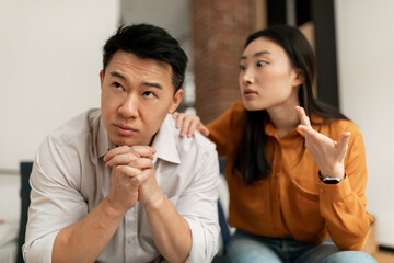 Fototapeta na wymiar Emotional chinese wife yelling and gesturing at middle aged husband, having difficulties in marriage