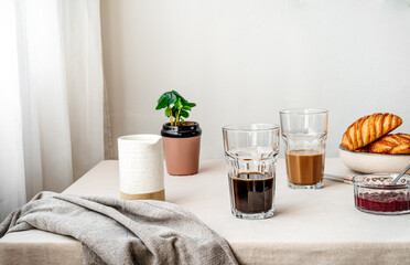Fototapeta na wymiar Spring cozy breakfast concept. Two glasses with coffee and milk, croissants, spring plant, jam, linen napkin. Kinfolk style