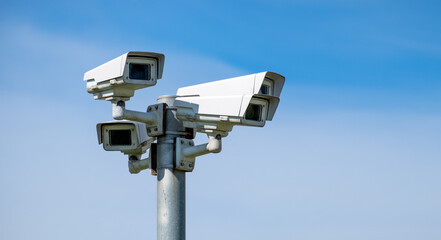 Four security cameras against the blue sky are monitoring. The image has a copy space.