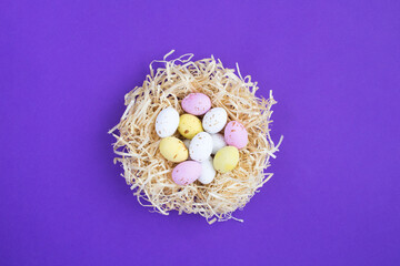 Colored easter eggs in a nest of straw on the purple background. Close-up. Top view.