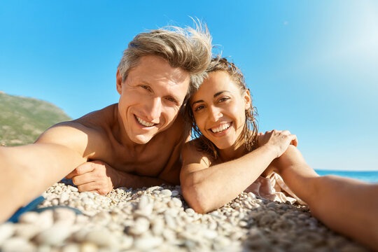 Happy couple in love lying on sunny beach, making selfie picture on romantic honeymoon holiday or vacation travel