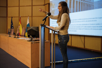 Middle-aged woman standing on the lectern to give a speech to her students during her graduation....