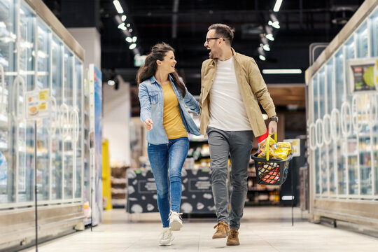 A happy couple is skipping and holding hands during purchase in hypermarket.