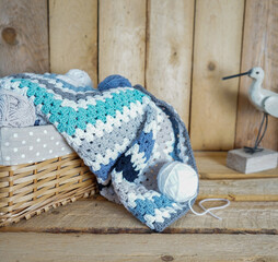Fototapeta na wymiar white, grey, blue granny square blanket with woolen balls in an white textile basket on wooden ground