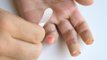 Man applying band aid patch on cuts wound on fingers. Male putting medical adhesive bandage tape sticking plaster to injured sore finger. First aid after accident, self cure help concept. Close-up