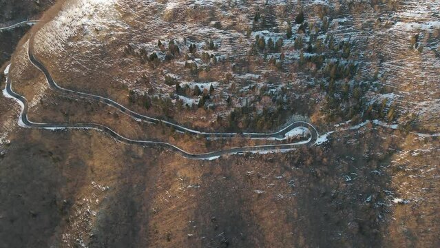 Aerial view of a scenic forest road on mountainside in wintertime at sunset with snow on Mount Terminio, Serino, Avellino, Irpinia, Campania, Italy.