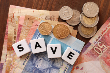 Concept of saving. South African currency the Rand with tile letters with the word save. Notes and coins 