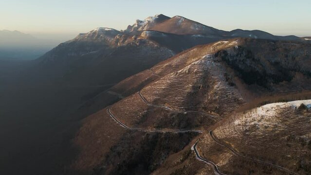 Aerial view of a scenic forest road on mountainside in wintertime at sunset with snow on Mount Terminio, Serino, Avellino, Irpinia, Campania, Italy.