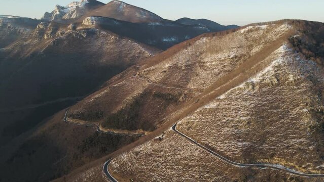 Aerial view of a scenic forest road on mountainside in wintertime at sunset with snow on Mount Terminio, Serino, Avellino, Irpinia, Campania, Italy.