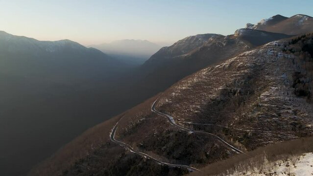 Aerial view of a scenic forest road on mountainside in wintertime at sunset with snow on Mount Terminio, Serino, Avellino, Irpinia, Campania, Italy.