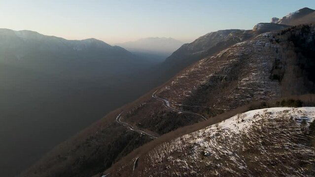 Aerial view of a scenic forest road on mountainside in wintertime at sunset with snow on Mount Terminio, Serino, Avellino, Irpinia, Campania, Italy.