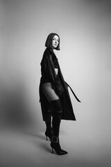 portrait of a young sexy woman in the studio on a white background in black boots and leather raincoat clothes.