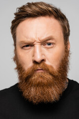 portrait of stringent bearded man frowning and looking at camera isolated on grey.