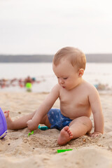 charming toddler sits in the sand and plays with toys on the seashore
