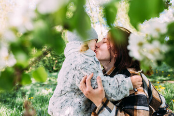 Young woman with her daughter in nature admires white flowering of spring trees