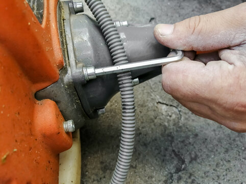 A man's hand repairs the instrument with a key. Repair of garden trimer. Key to repair the trimer motor.