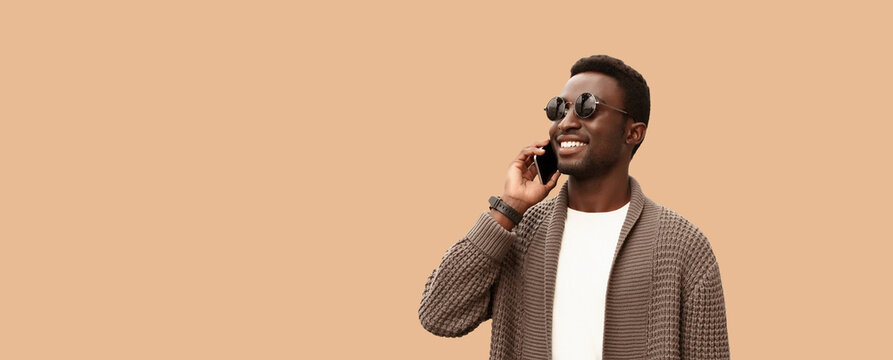 Portrait of happy smiling young african man calling on smartphone isolated on brown background, copy space