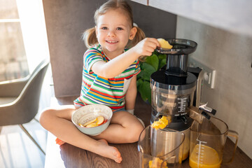 Little girl making fresh juice sitting on the table in home kitchen