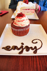 Red Velvet Cupcake Plated with the Word “Enjoy” in Icing on a White Square Plate