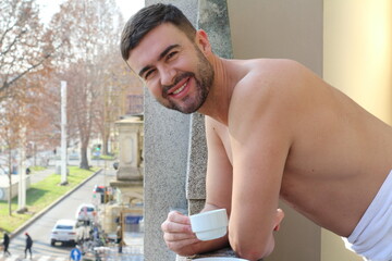 Attractive shirtless man drinking a coffee in the balcony 