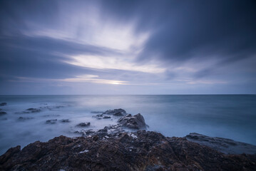 Long exposure shot of rocks on seaside, blurred and foggy sea water and clouds on sky