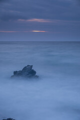 Long exposure shot of rocks on seaside, blurred and foggy sea water and clouds on sky