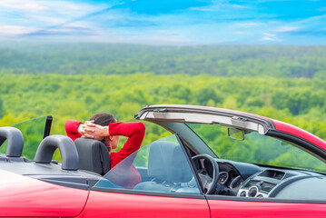 Woman in red car with open roof at background of sea water.