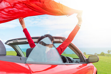 Woman in red car with open roof at background of sea water.