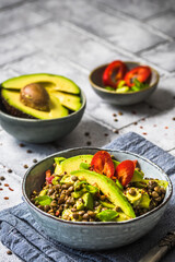 Lentil salad with avocado and red pepper on gray tiles background.  Vegetarian and vegan food. Vertical.