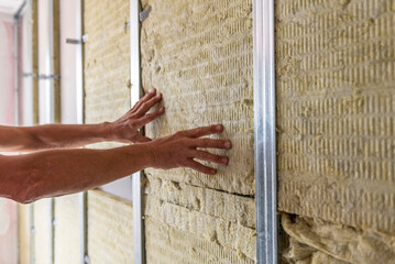 Worker insulating a room wall with mineral rock wool thermal insulation. - obrazy, fototapety, plakaty