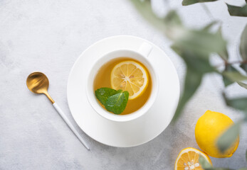 Herbal tea with lemon and mint in a white cup on a light background with eucalyptus branches close up. The concept of a healthy and delicious breakfast drink for immunity. © Ольга Кучкина