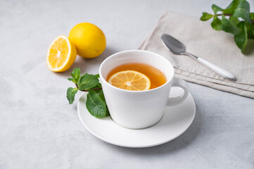 A cup of tea with lemon and mint on a light background. The concept of a healthy breakfast drink