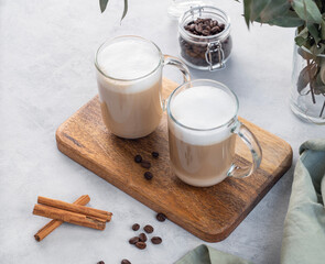Two cappuccino or latte with milk foam in glasses on a light background with coffee beans, cinnamon and eucalyptus branch.