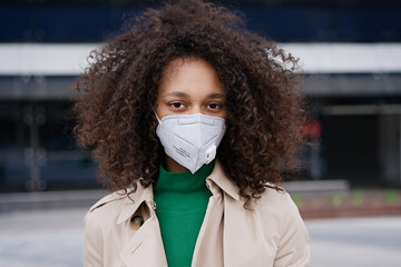 Young african woman girl in wearing face mask ffp2 walking outdoors carrying a suitcase and going...