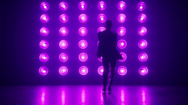 Silhouette of talented young hip hop dancer. Hip hop or RnB street dance on stage in dark studio with smoke and neon ultra violet lighting. Bulb light wall studio background. Creative skills performer