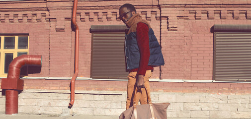 Stylish young african man model posing wearing sweater with bag on city street background