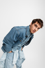 stylish young man in denim clothes posing with hands in pockets and looking at camera isolated on grey.