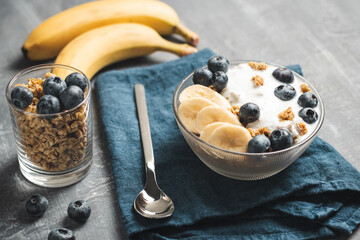 Granola cereal oatmeal with white yogurt, blueberries and banana fruits in a bowl on a blue napkin,...