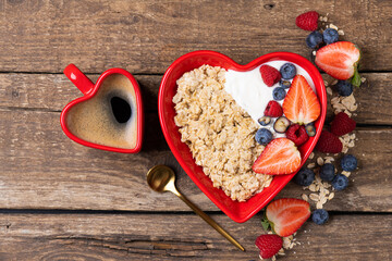 Oatmeal porridge with berry and yogurt in red bowl in the heart shape. Oat flakes healthy breakfast meal with coffee cup. Valentine day concept. Top view