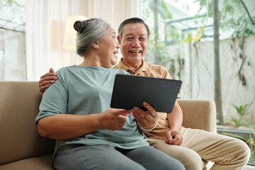 Joyful senior couple watching funny videos on tablet computer