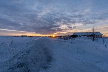 Secluded house in the snow with the ground and the road completely snow covered and the sun rising over the horizon in a residential area of Selfoss in Iceland with the cloudy sky illuminated